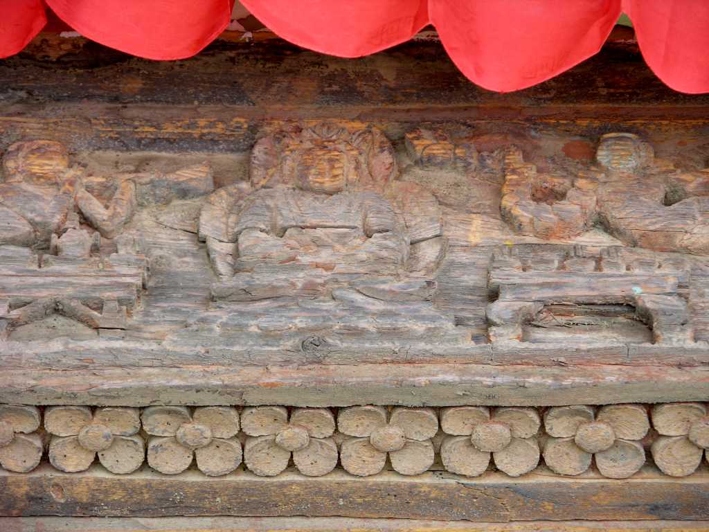 Tibet Guge 07 Tsaparang Red Temple 03 Door Carving Its pillars are sculpted with floral motifs and covered up with small figures worked out with great delicacy  Above, in a square frame, the Buddha seated in the posture of meditation; on his sides two small figures of gods who hovering in the air play the trumpet by way of homage. - Giuseppe Tucci: The Temples of Western Tibet and their Artistic Symbolism (1935).